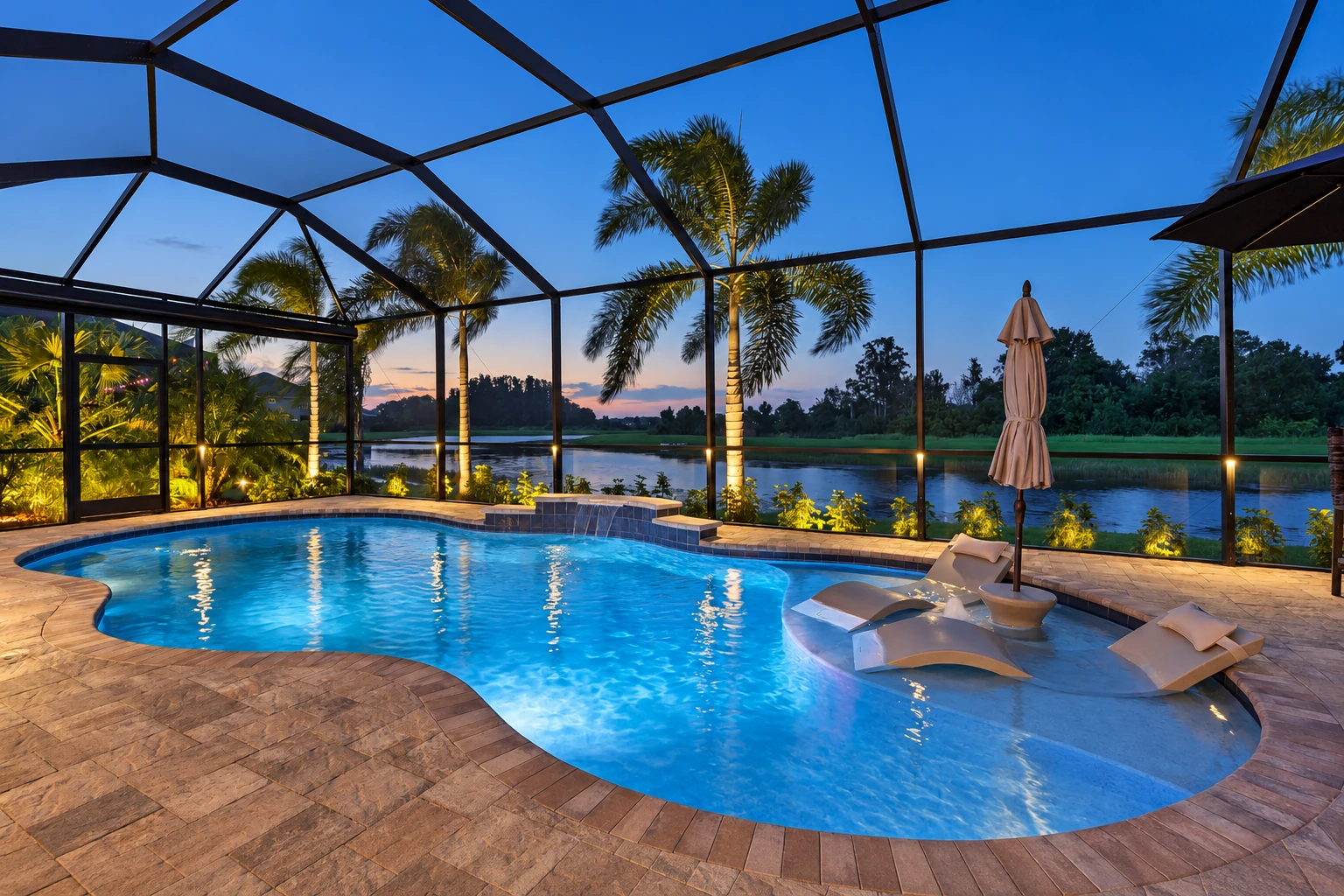 Enclosed patio room with a screened roof surrounds a curving swimming pool, lounge chairs, and a waterside view at dusk.