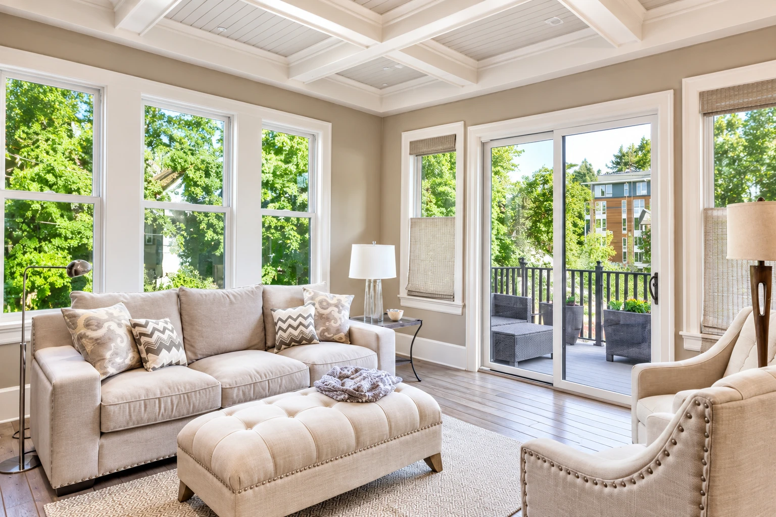 Sunroom with exposed white ceiling beams, large windows, sliding glass doors, and a beige sofa facing a deck.